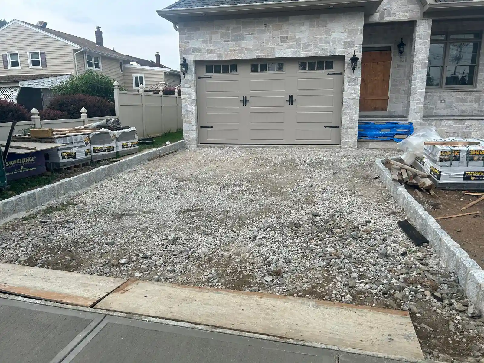 Front view of a two-story house with driveway construction going on, a stone facade and a double garage