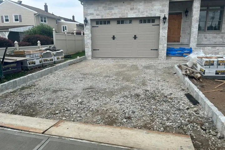 Front view of a two-story house with driveway construction going on, a stone facade and a double garage