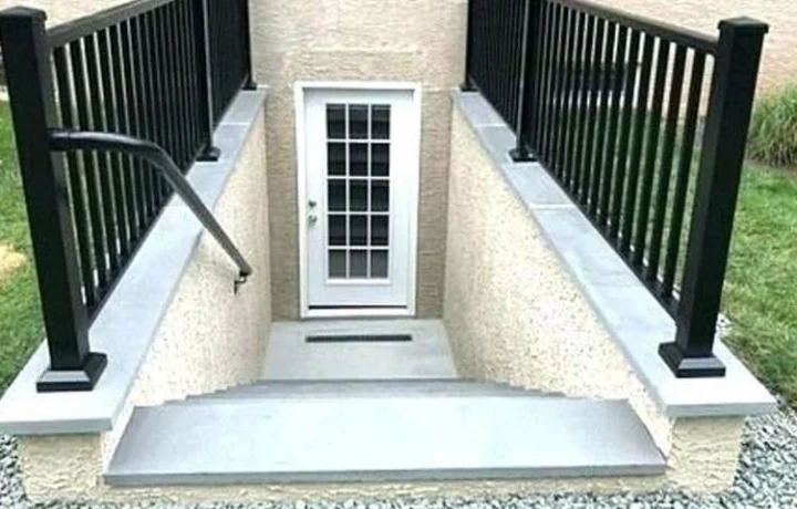 Outdoor staircase with black metal railings leading down to a white door, surrounded by gravel and grass