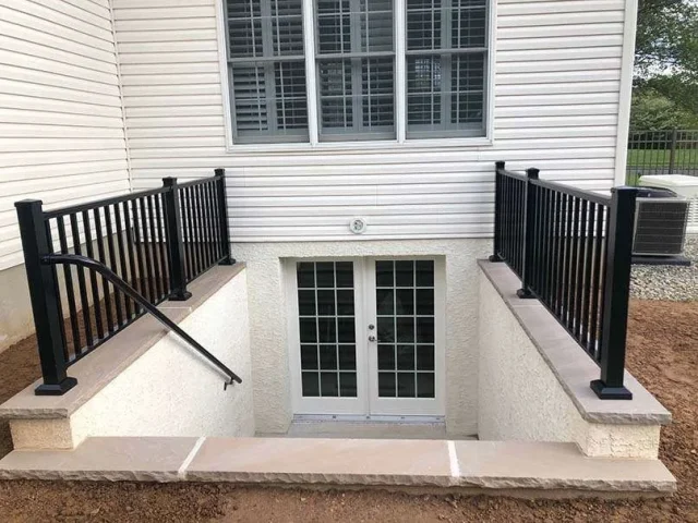 Exterior basement entrance with white door, sidelights, and black metal railings