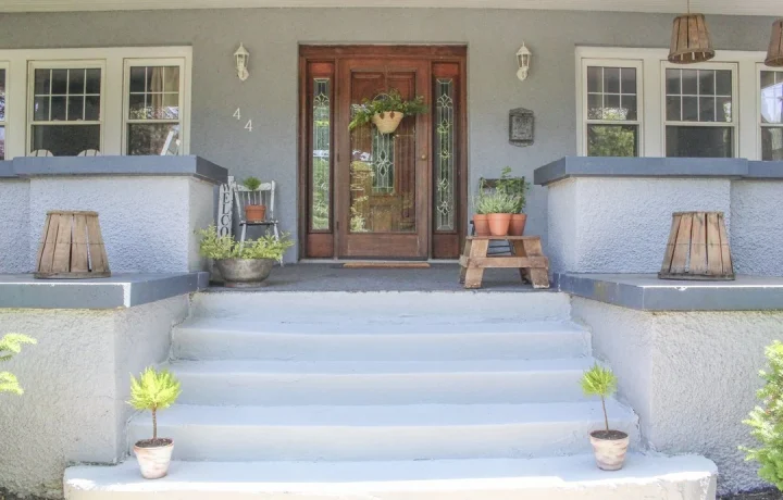 Front entrance of a house with steps leading up to a wooden door with glass panels, blue walls, and potted plants