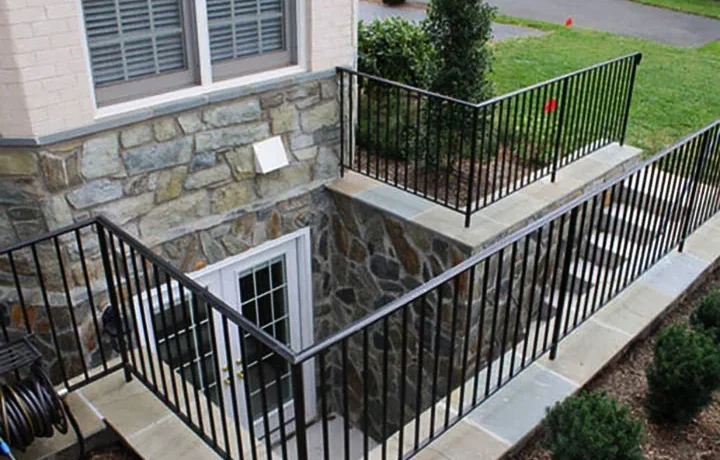 Side entrance to basement with black metal stairs and railing, leading to a white door