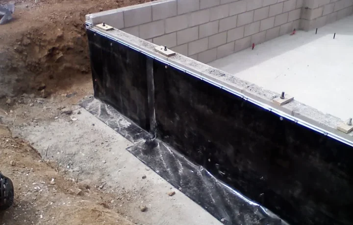 Construction site with black waterproofing membrane applied to foundation wall