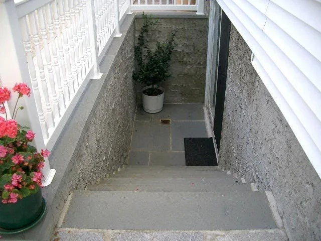 Concrete steps leading down to a basement entrance with white railing and potted plants