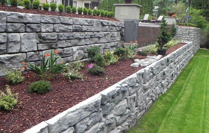 Tall retaining wall constructed with grey stones and garden bed