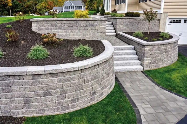 Curved retaining wall made of interlocking stone blocks with stairs and garden beds