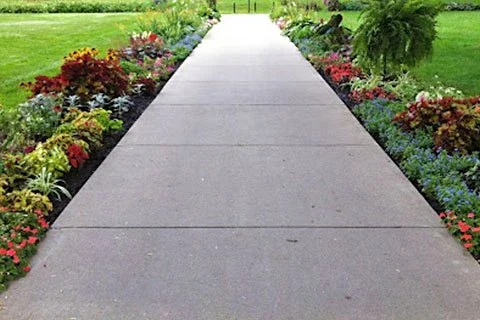 Concrete walkway through a well-manicured lawn with vibrant flowerbeds on both sides