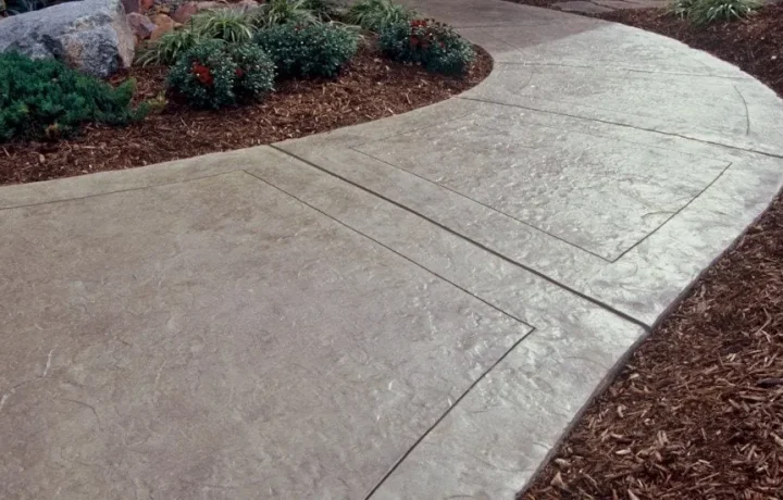 Curved concrete pathway with smooth finish in a landscaped garden with shrubs and mulch